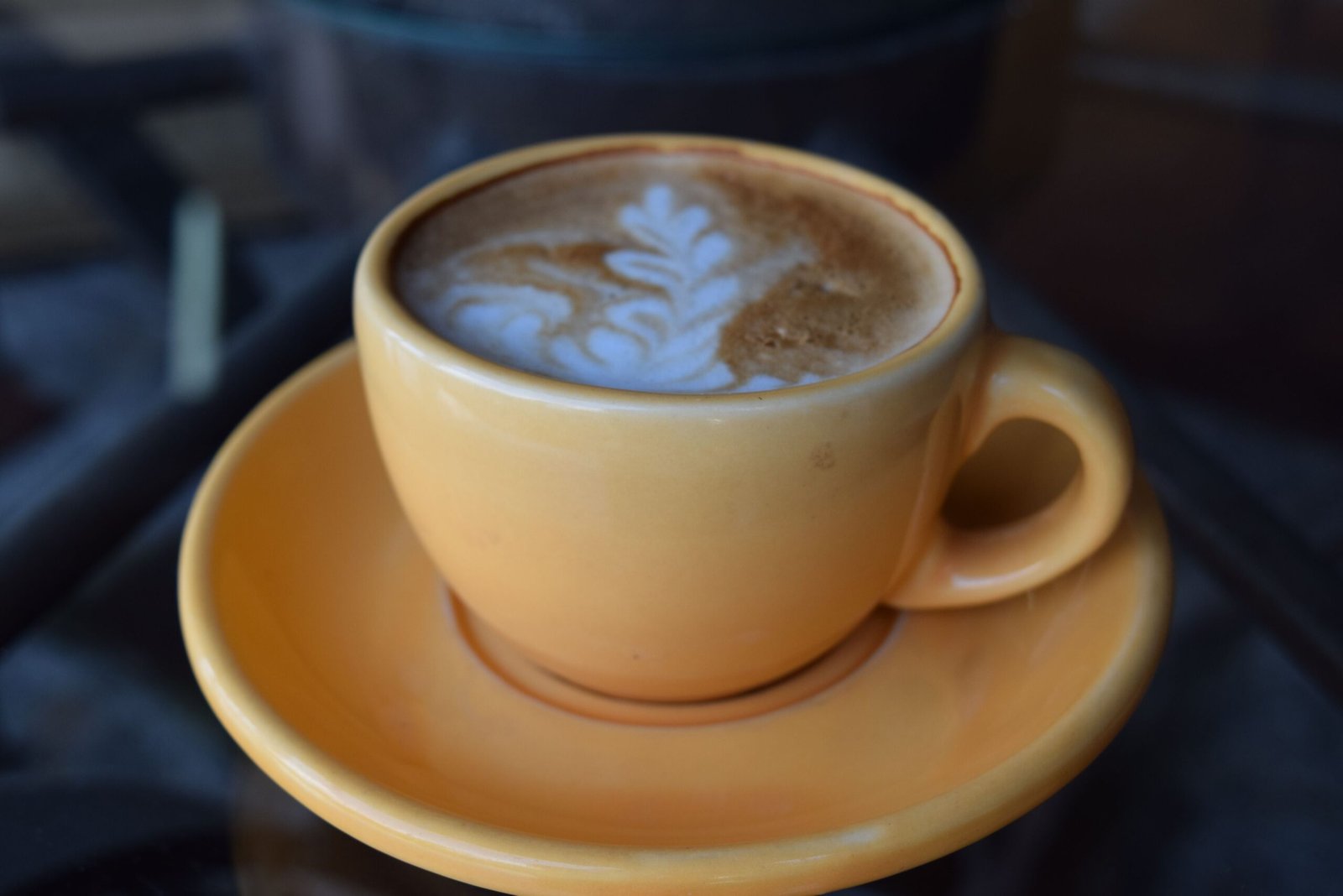 Capture of a latte with intricate art, served in a yellow cup on a table.