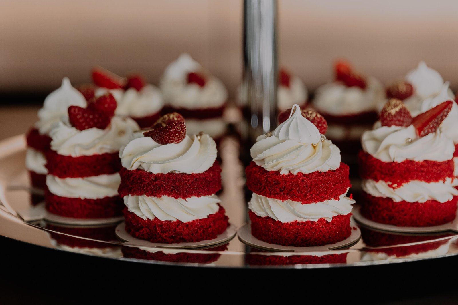 Close-up of red velvet mini cakes topped with whipped cream and strawberries on a tray.