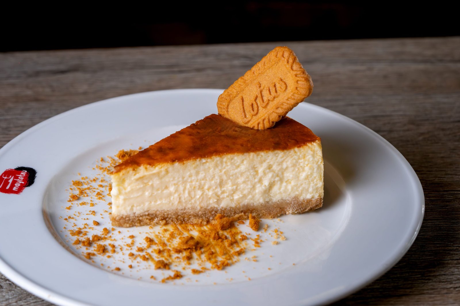Tasty cheesecake slice topped with a Lotus biscuit on a white plate.