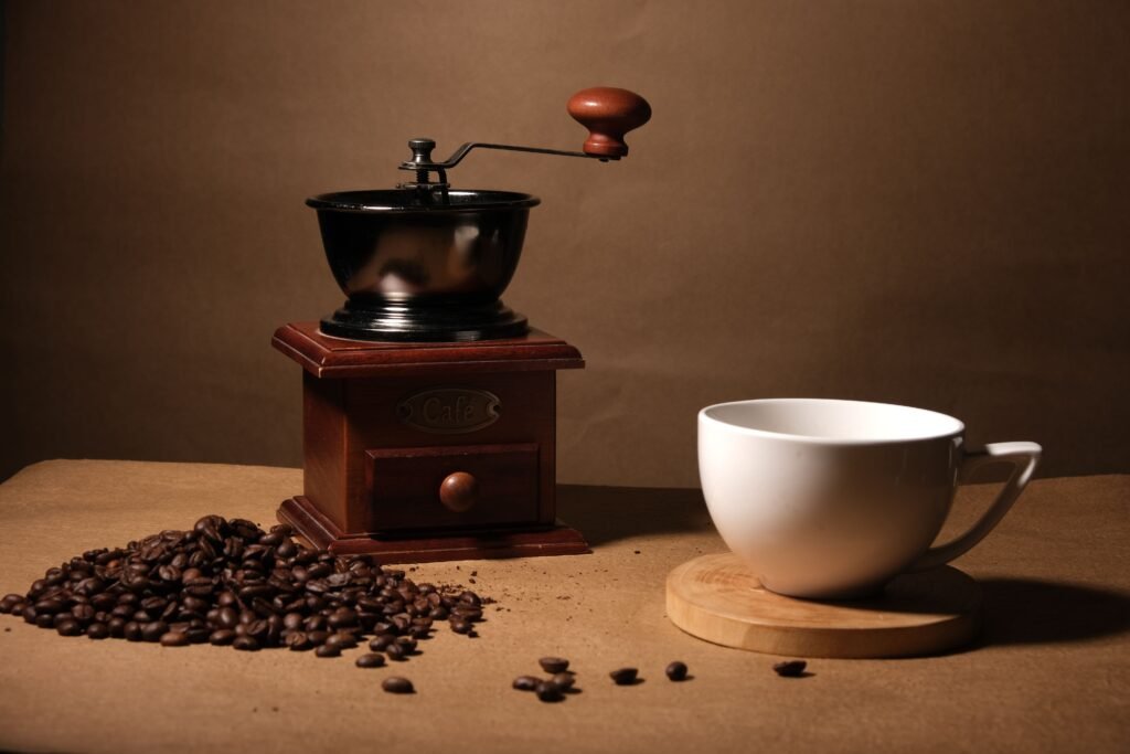 A vintage coffee grinder, coffee beans, and a white mug on a wooden surface, rich with warm tones.