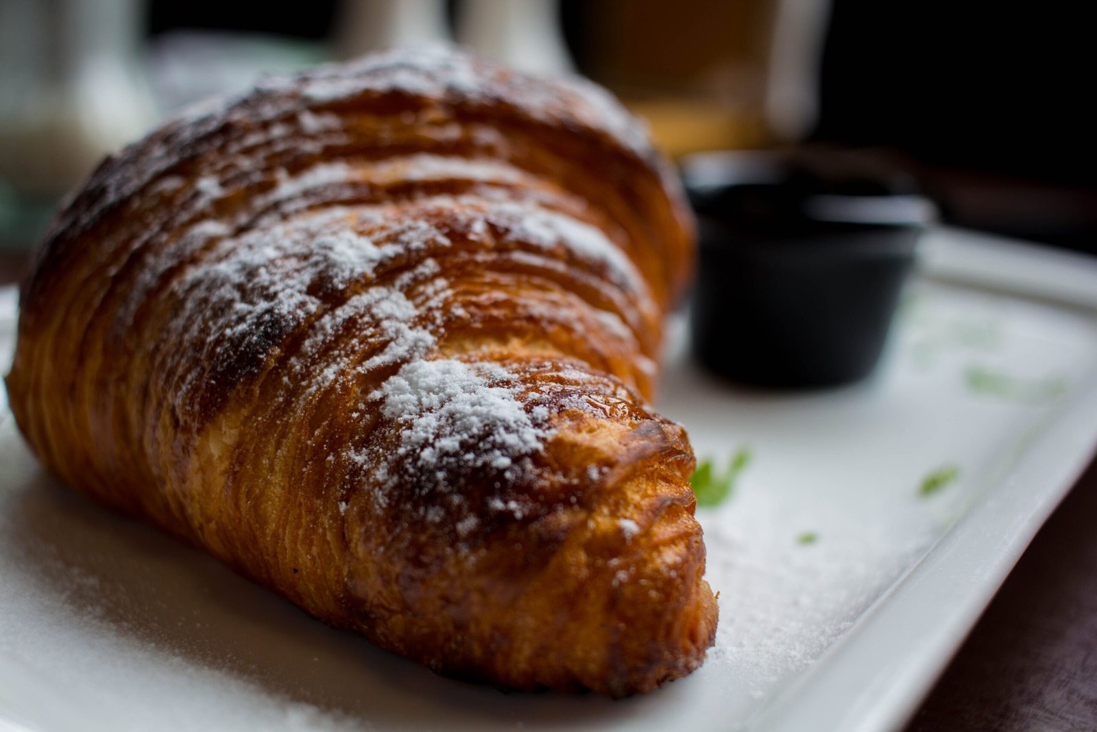 Close-up of a flaky croissant dusted with powdered sugar, served on a plate.